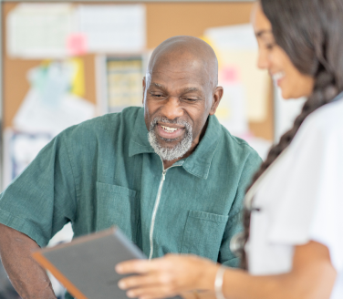 Physician assistant in a white coat reviewing a tablet together with patient.