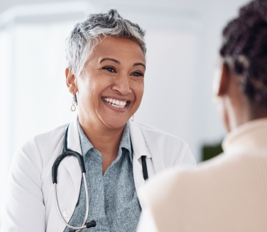 Healthcare provider in a white coat and stethoscope smiling during a conversation at an employee health center