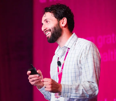 Dr. Levi Rizk speaking on a pink-lit stage at a conference event.