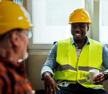 Two union workers in hard hats and safety vests having a conversation in an office setting.