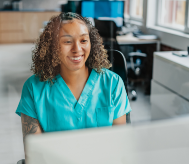 Referral coordinator smiling while working at a computer in a clinic office.