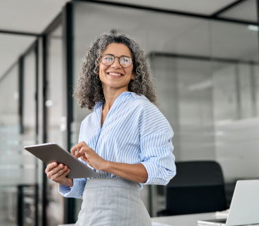 Person wearing glasses holding a tablet and smiling in a modern office setting