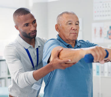 An MSK professional guides a person through a dumbbell arm exercise in a clinical setting during a musculoskeletal session.