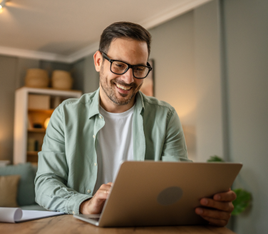 Person smiling while using a laptop at a home desk during a virtual care session.