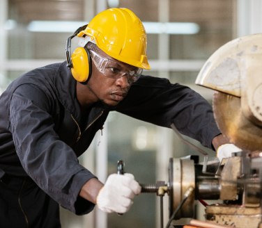 Worker in a yellow hard hat, safety glasses and gloves operates industrial machinery