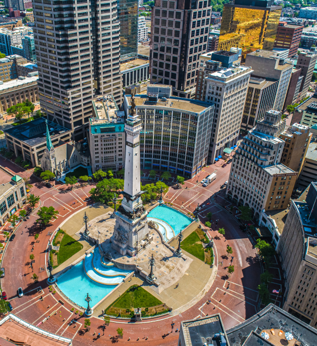 Aerial view of a downtown city monument with fountains, a tall column, and surrounding skyscrapers