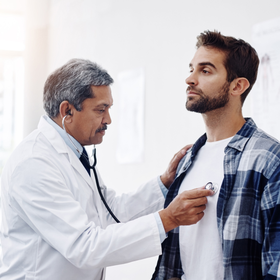 A healthcare provider in a white coat uses a stethoscope to examine a Bendix employee in a plaid shirt in a clinical setting