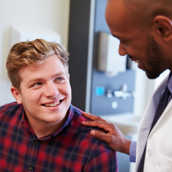 A Briggs & Stratton employee in a plaid shirt looks up at a white-coated healthcare provider resting a hand on their shoulder.