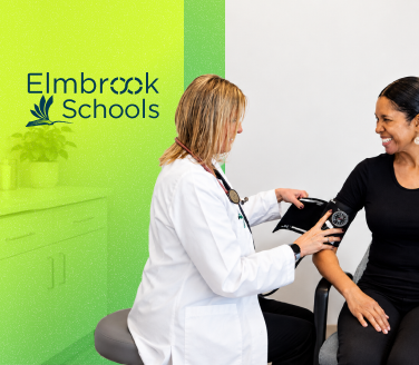 Elmbrook Schools healthcare provider in white coat applying a blood pressure cuff on a smiling person