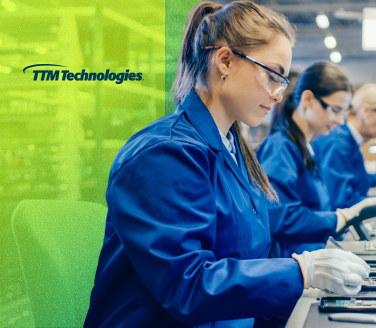 TTM Technologies workers in blue lab coats and safety glasses assemble components on a production floor