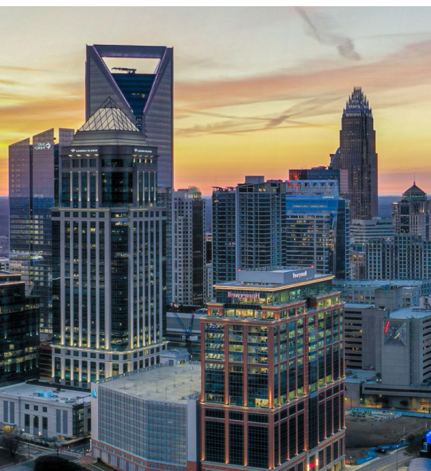 Charlotte city skyline at sunset with illuminated high-rise buildings beneath an orange and gold sky