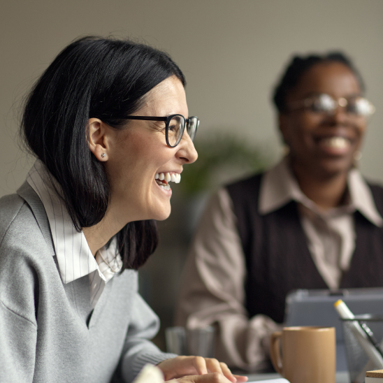 Two people smiling during a meeting at a desk with a mug and tablet visible nearby
