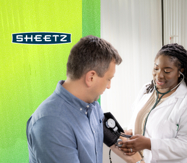 A healthcare provider in a white coat uses a blood pressure cuff on a person at a Sheetz facility