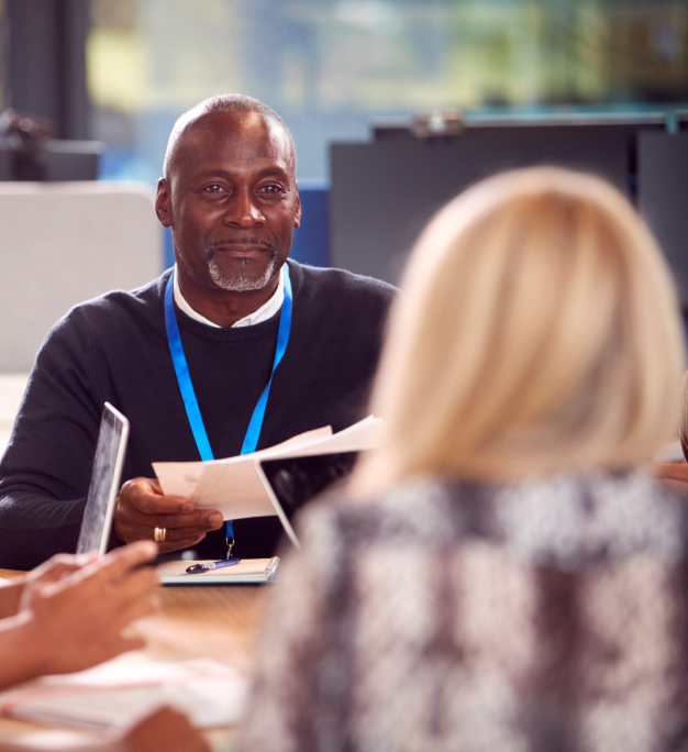 Person wearing a blue lanyard holds documents across a table from another person in an office setting