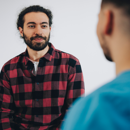 Person in a red plaid shirt smiling during a conversation with a healthcare provider in blue scrubs