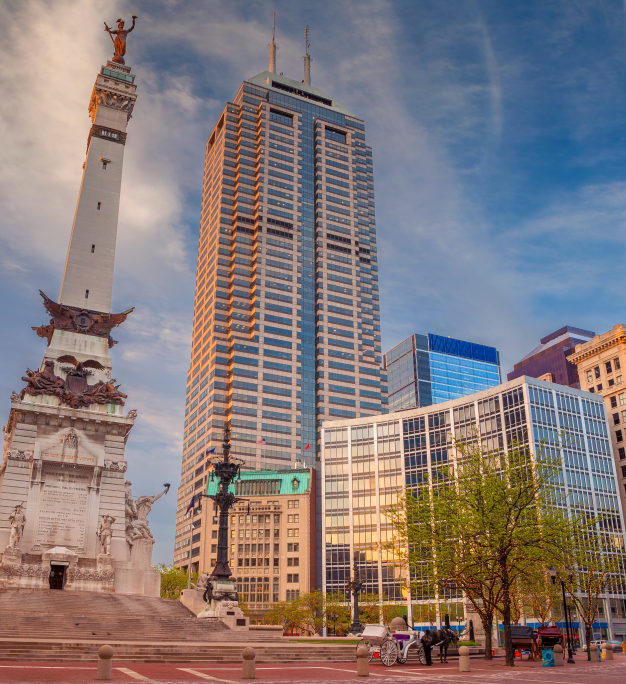 Downtown Indianapolis skyline featuring the Soldiers and Sailors Monument and a tall glass skyscraper under blue skies