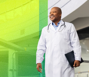 Smiling healthcare provider in a white coat and stethoscope walking and holding a folder outdoors
