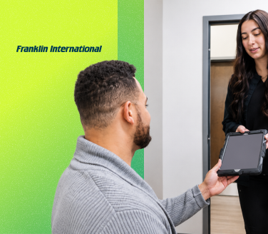 Franklin International professional hands a tablet device to a seated person near a doorway