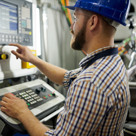Person in a blue hard hat and plaid shirt operating an industrial control panel in a manufacturing facility