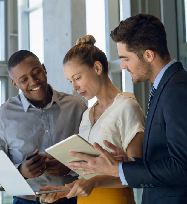 Three professionals gathered together reviewing content on a tablet and laptop in a bright office setting
