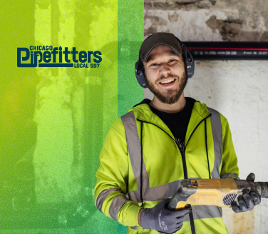 Smiling Local 597 Pipefitters worker in hi-vis jacket and ear protection holding a power drill at a worksite