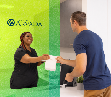 A healthcare provider in scrubs hands paperwork to a person at a City of Arvada health center front desk