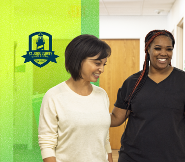 Two people walking together in a hallway with the St. Johns County School District logo visible on a green background