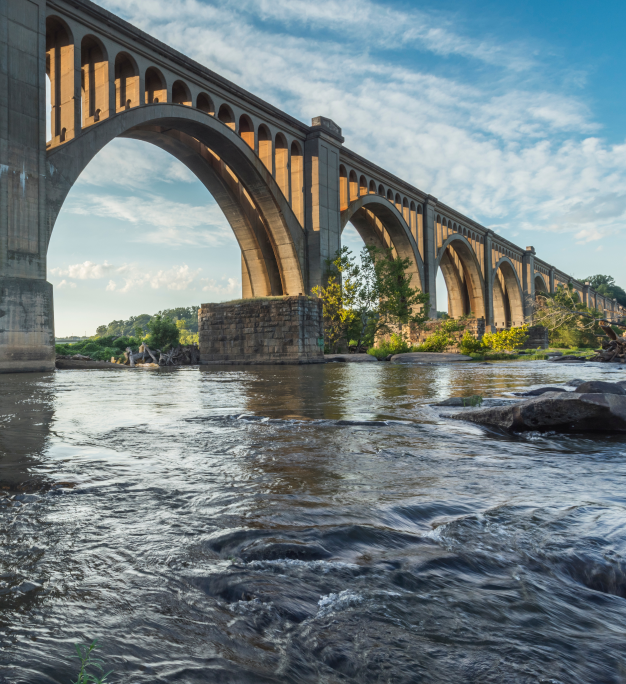 Arched concrete railway bridge spanning a rocky river under a partly cloudy sky