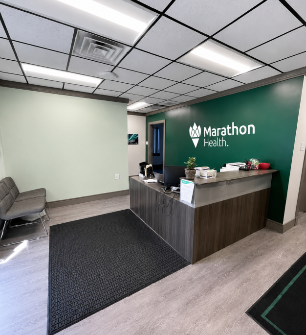 Marathon Health reception desk with a green accent wall, logo signage and waiting-area seating