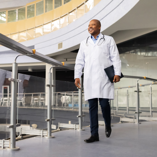 Provider in a white coat carrying a folder walks through a bright atrium