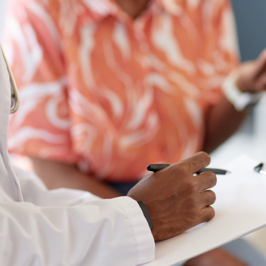 Healthcare provider in a white coat writing on a clipboard during a one-on-one consultation with a person.