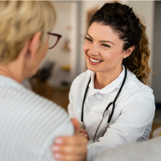 A smiling healthcare provider with a stethoscope engages warmly with a person during a one-on-one conversation