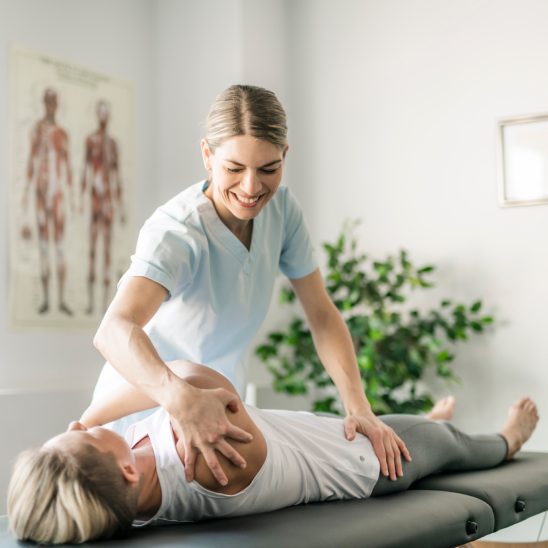 Smiling healthcare provider in scrubs works with a person lying on a treatment table in a bright clinical room