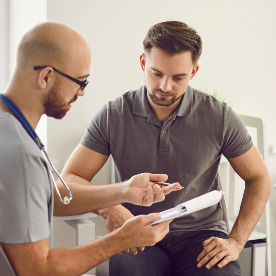 Healthcare provider with stethoscope reviews clipboard documents with a person seated in a bright clinical room
