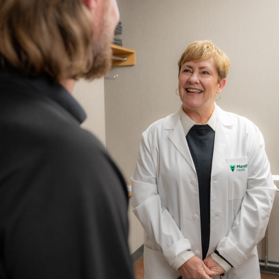 Marathon Health provider in white coat smiling while speaking with a person in an indoor clinic setting