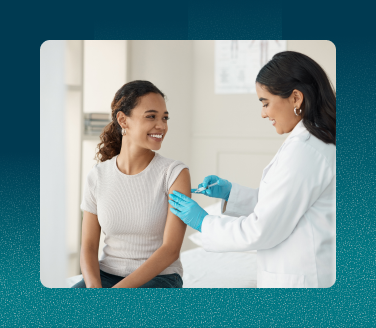 Healthcare provider in a white coat and blue gloves administering a flu shot to a person in a clinic setting.