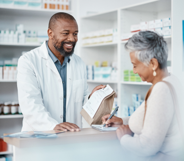 Pharmacist holds a paper bag while a person signs a form at a pharmacy counter