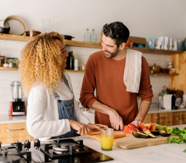 Two people chop vegetables together at a kitchen counter with a glass of orange juice nearby