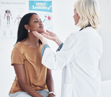 Provider in a white coat gently examines a seated person's neck in an exam room