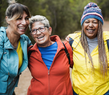Four older women people in colorful jackets stand arm in arm on an outdoor trail