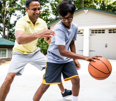 Two people play basketball on a driveway in front of a garage