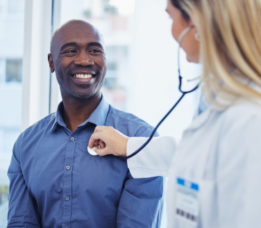 Provider listens with a stethoscope to the chest of a smiling person in a blue shirt