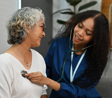 Provider in blue scrubs listens with a stethoscope to a smiling person's chest