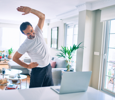 Person does a standing side stretch beside a laptop in a bright living room