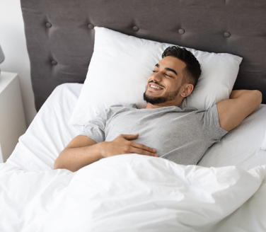 Person smiling with eyes closed while lying back on a pillow in bed