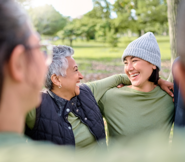 Two people in knit hats laugh together with friends in a park