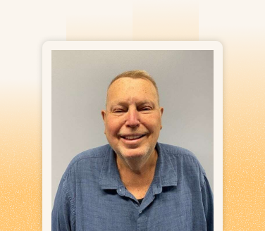 Bob Brennan smiling in a blue button-up shirt against a neutral gray background