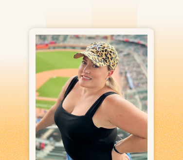 Rachel Strouse smiling at a baseball stadium, wearing a black tank top and leopard-print cap
