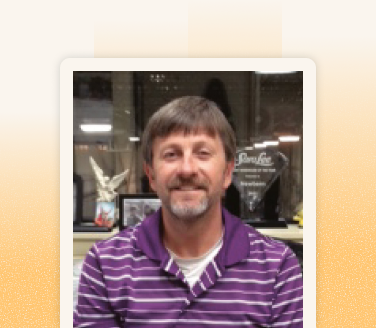 Craig Borden smiling in a purple striped polo shirt, seated in an office with awards and framed photos visible behind him