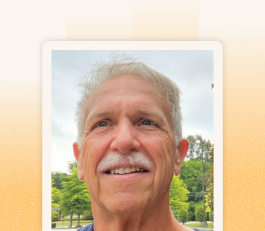 Ron Boyd smiling outdoors with trees and a cloudy sky visible in the background